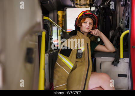 Image de firewoman gingembre à la caméra en séance dans la cabine du camion de pompiers Banque D'Images