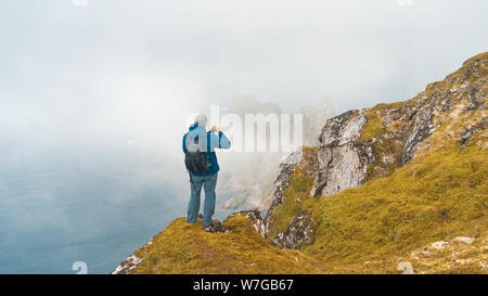 Aventurier solitaire cherche dans le paysage et écouter le silence. Photographe assis sur falaise, relaxant. Avec vue sur montagne nuages Banque D'Images