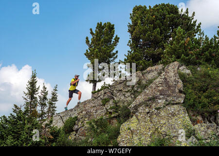 Runner mâle tournant sur un sentier de montagne. Exécute l'athlète dans les montagnes au milieu des rochers. Homme dans un T-shirt jaune et un short noir est en formation pis Banque D'Images