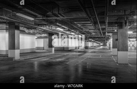 Grungy, faiblement éclairées garage parking vide avec éclairage vertical et un panneau de sortie qui pendent du plafond. Banque D'Images