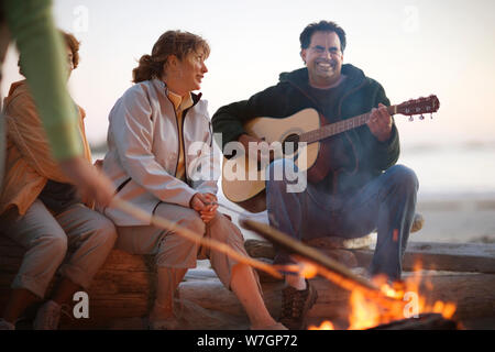 Famille assis autour d'un feu de camp et les guimauves grillage playing guitar Banque D'Images