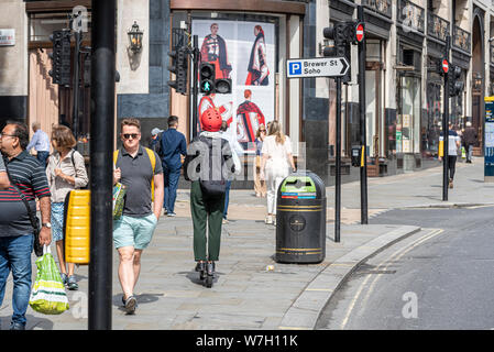 La femme un scooter électrique sur le trottoir à Londres à proximité d'un certain nombre de piétons en marche. Les gens sur occupation de la chaussée. Vue arrière, pas de visage de rider Banque D'Images