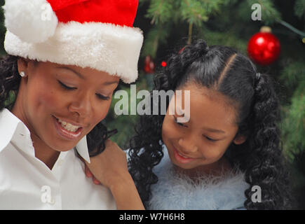 Mère et fille portant des chapeaux de Père Noël assis autour de l'arbre de Noël enveloppant des cadeaux Banque D'Images