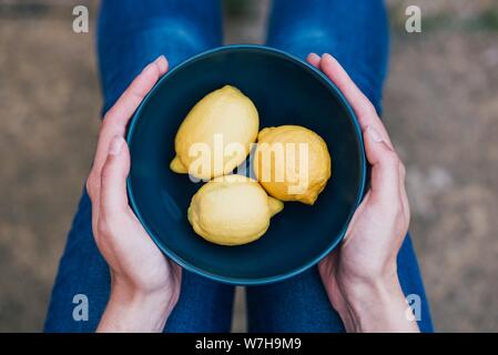 Gros plan de citrons jaunes dans un bol bleu maintenu par une femme Banque D'Images