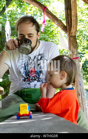 Kharkiv, Ukraine - Juillet 09, 2019 : un jeune homme alimente un petit garçon avec une cuillère d'un mug, père et fils à l'extérieur Banque D'Images