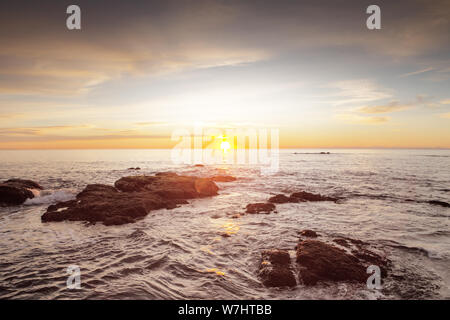 Lever du soleil à venir sur la mer avec les vagues se briser contre les rochers sur la côte de Benalmadena espagne Banque D'Images