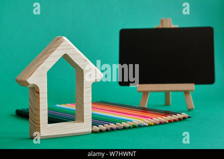 Une maison en bois, figurine, miniature tableau sur un chevalet et crayons de couleur fixés par les couleurs arc-en-ciel d'isoler sur fond vert, concept à s Banque D'Images