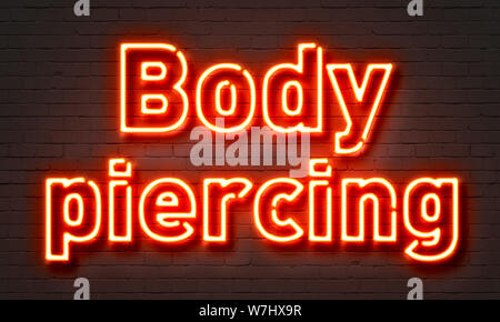 Body piercing neon sign on brick wall background Banque D'Images