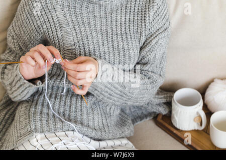 Jeune fille dans un chandail gris chaud tricote assise sur un canapé dans un intérieur cosy hygge Banque D'Images