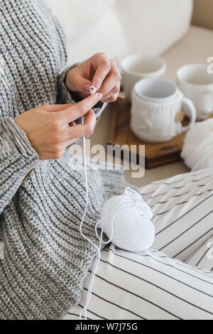 Jeune fille dans un chandail gris chaud tricote assise sur un canapé dans un intérieur cosy hygge Banque D'Images