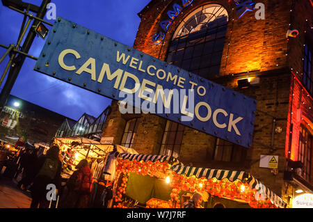 Entrée de Camden Lock. Grand panneau bleu 'Bienvenue à Camden Lock', à l'entrée du marché. En début de soirée, l'éclairage orange chaud et occupé dans les étals de marché. Banque D'Images