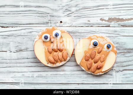 Pour les enfants de nourriture drôle. Gâteaux de riz en forme de hiboux allongé sur un tableau blanc rustique. Fait à partir de beurre d'arachide, des tranches de pomme, les amandes, les bonbons et les baies. Banque D'Images