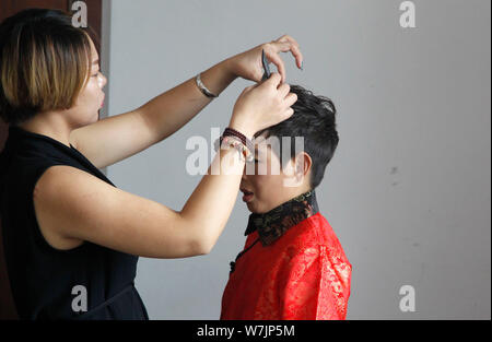 42 ans époux chinois Li Haimin habillés en costumes traditionnels, la droite, qui est de 4 pieds 8 pouces de haut, termine ses cheveux et maquillage avec le il Banque D'Images