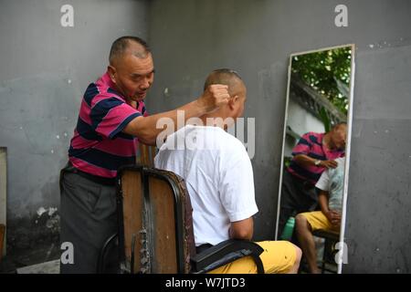 Un client se couper les cheveux par la 62-year-old coiffure chinois Xiong Gaowu à sa coupe de l'extérieur, wc séparés dans une ruelle à Jinjiang District, Chengdu City Banque D'Images