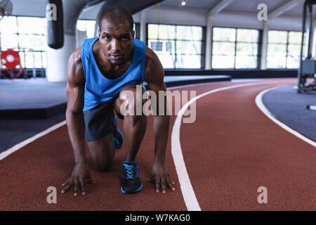 Homme athletic en position initiale sur une piste de course dans le centre de remise en forme Banque D'Images