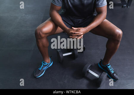 Homme assis avec les mains jointes sur un banc dans le centre de remise en forme Banque D'Images