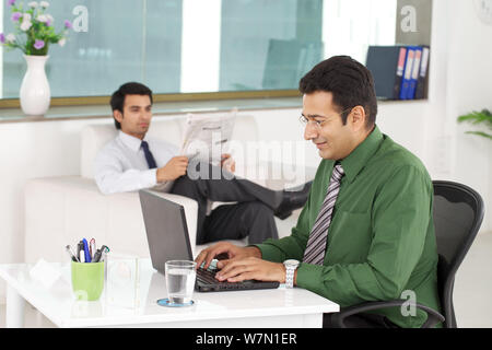 Conseiller financier travaillant sur un ordinateur portable avec un client en attente en arrière-plan Banque D'Images