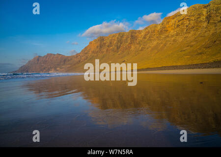 L'Espagne, Lanzarote, d'énormes montagnes de Famara massif reflète dans la plage de Famara au coucher du soleil Banque D'Images