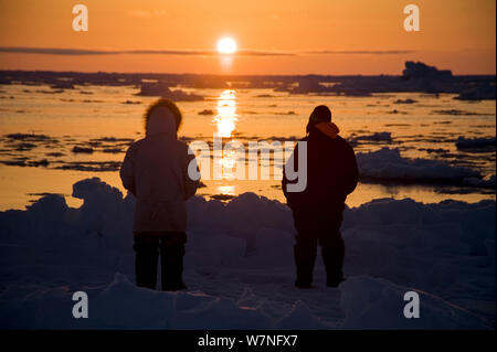 Silhouette d'Inupiaq baleiniers de subsistance au bord d'une coupure dans la banquise, à passer les baleines boréales comme le soleil de midi suit l'horizon. Mer de Tchoukotka, au large de Barrow, côte de l'Arctique de l'Alaska, mai 2012. Banque D'Images