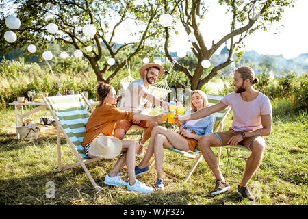 Les jeunes et joyeux amis se détendre sur les chaises longues, dans clinking glasses l'arrière-cour ou jardin magnifiquement décorée lors d'une réunion festive Banque D'Images