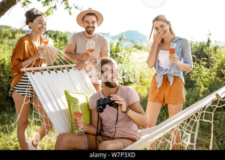 Jeunes amis de s'amuser à la recherche avec des jumelles, assis sur le hammmock sur l'arrière-cour ou le jardin lors d'une réunion festive sur le coucher du soleil Banque D'Images