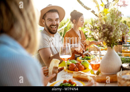 Les jeunes gens heureux et avoir déjeuner festif à la table magnifiquement décorée avec des aliments sains dans le jardin Banque D'Images