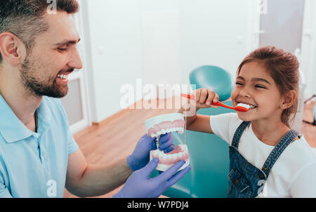 Enseignement dentiste peu mixed race girl se brosser les dents à l'aide de dents humaines modèle à une clinique dentaire Banque D'Images