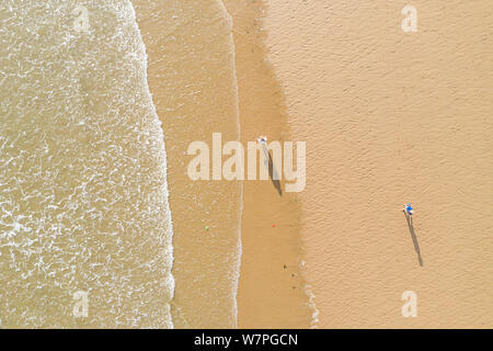 Vue aérienne de personnes à pied et leur ombre sur une plage de sable à côté des vagues dans Porthcawl au Pays de Galles UK Banque D'Images