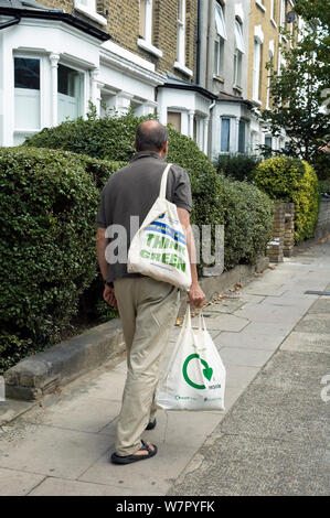 Homme marchant le long de la rue urbain transportant deux sacs en coton réutilisables avec le logo imprimé sur l'un et pense que verte de l'autre, Holloway, Département du Nord-Ouest, Angleterre, Royaume-Uni, Septembre 2006 Banque D'Images