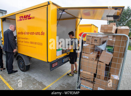 Wittenburg, Allemagne. 07Th Aug 2019. Christian Pegel (SPD), l'énergie et le ministre des Transports, de Mecklembourg-Poméranie occidentale, observe une femme Deutsche Post livraison de colis pré-tri des lots à travers le volet de chargement d'un 'street', un transporteur électrique. Pegel peuvent en savoir plus sur l'utilisation de l'électromobilité au Deutsche Post DHL. Des 14 300 véhicules exploités par la Poste suisse dans toute l'Allemagne, autour de 9 000 camionnettes de livraison sont à commande électrique. En plus de l'treetscooter', 3 000 e-bikes sont également en cours d'utilisation. Credit :/dpa/Alamy Live News Banque D'Images