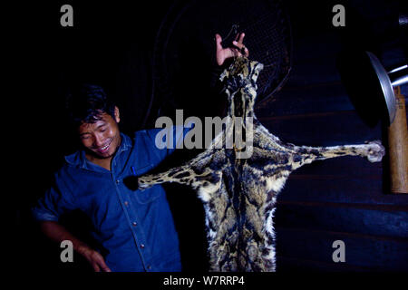 Naga homme tenant la peau d'une panthère nébuleuse (Neofelis nebulosa) à l'intérieur d'une cuisine, d'Shatuza, Nagaland, l'Inde, 2011. Banque D'Images