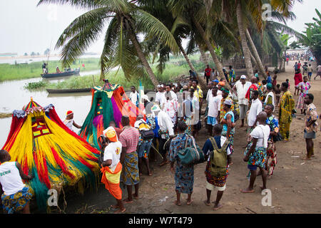 Regarder les hommes', 'Zangbeto voodoo traditionnels gardiens de la nuit dans la religion Yoruba, sont aidés à en bateau vers un autre village pour Voodoo / cérémonie vodoun, Bénin, février 2011. Banque D'Images