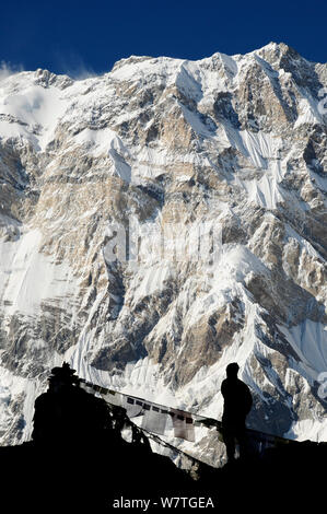 Mount Annapurna I (8091m) à partir du camp de base, avec des drapeaux de prière et randonneur silhouetté, sanctuaire de l'Annapurna, Népal central, novembre 2011. Banque D'Images