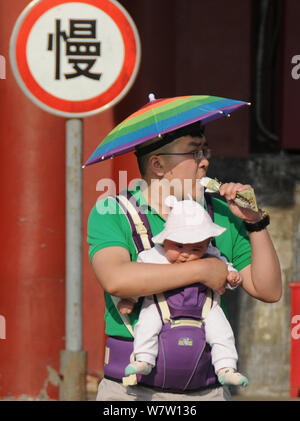 Un blindage touristique lui-même avec un chapeau du soleil de plomb mange une glace et porte son bébé comme il visite la place Tian'anmen à Beijing, Ch Banque D'Images