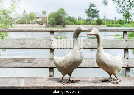 Un couple d'oie blanche, debout sur un pont de bois près de la rivière, une statue de deux oies sur une journée ensoleillée Banque D'Images