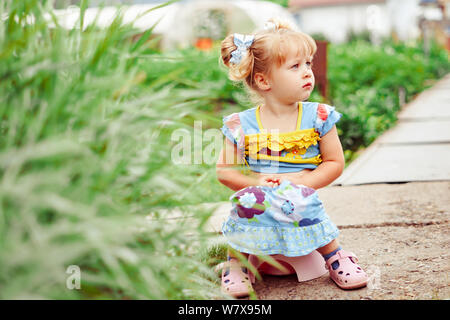 Portrait of cute little girl sitting on petit pot à l'extérieur Banque D'Images