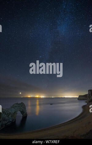 Stars et Milky Way plus de Durdle Door et la Côte Jurassique, avec les lumières de l'au-delà de Weymouth et Portland, Dorset, Angleterre, Royaume-Uni, décembre 2013. Banque D'Images