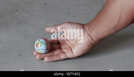 Petit globe on part avec l'arrière-plan de béton gris vu de profil. Monde dans nos mains avec enironmental la conservation. Banque D'Images