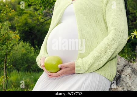 Partie du corps Pregnant belly et hand holding green apple avec robe blanche Selective focus Banque D'Images