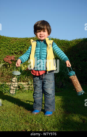 Jeune garçon se balançant deux mangeoires jardin rempli d'arachides et de boules de graisse avant de les accrocher, Bristol, Royaume-Uni, octobre 2014. Parution du modèle. Banque D'Images