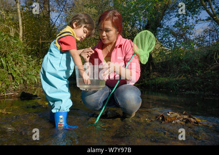 Jeune garçon dans un réservoir en plastique tenu par sa mère pour l'étang d'escargots qu'il a pris alors que la pêche en ruisseau, Bristol, Royaume-Uni, octobre 2014. Parution du modèle. Banque D'Images