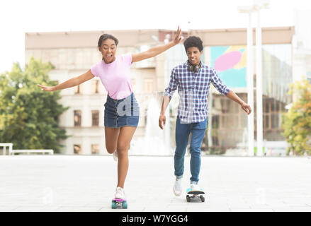 Teenage couple riding modern cruiser skateboards on city street Banque D'Images