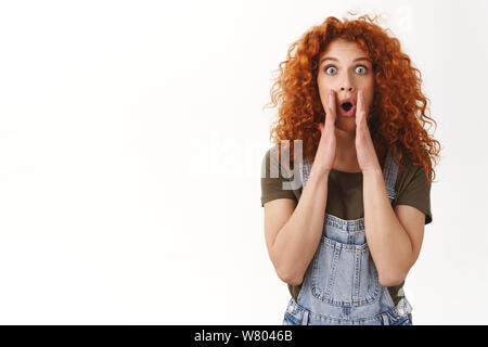 Incroyables d'alerte, qu'il entende. L'étonnement excités ginger girl aux cheveux bouclés yeux popping excité de l'appareil photo, tenez les mains près de la bouche ouverte pour crier lo Banque D'Images