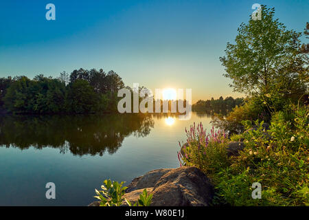 Coucher du soleil sur un lac avec l'eau et le ciel bleu, dans l'avant-plan la sauge et pierres rondes Banque D'Images