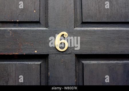 Numéro de maison 6 de bronze avec les six centrée sur une vieille porte en bois noir Banque D'Images