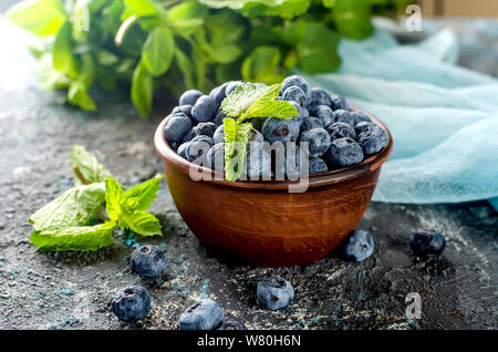 Les bleuets mûrs en ceramik bol avec menthe feuilles sur un fond de béton foncé Banque D'Images