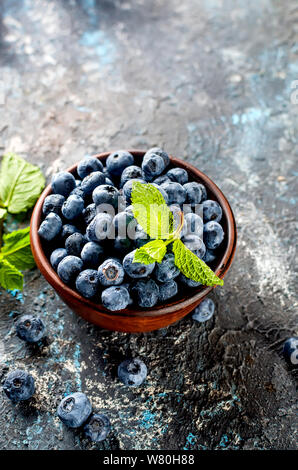 Les bleuets mûrs en ceramik bol avec menthe feuilles sur un fond de béton foncé Banque D'Images