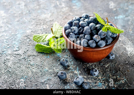Les bleuets mûrs en ceramik bol avec menthe feuilles sur un fond de béton foncé Banque D'Images