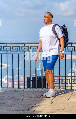 Athletic Senior man with backpack debout sur littoral et bénéficiant d'une vue imprenable sur la mer. Voyageant le long de la côte, de liberté et de vie actif concept.business man avec bronzage sain en vacances. Banque D'Images