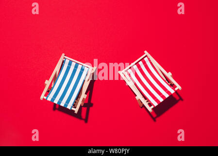 Deux chaises longues avec disque ombre sur papier rouge arrière-plan. Mise à plat et de copier l'espace. Été voyage vacances concept. Composition minimale. Banque D'Images